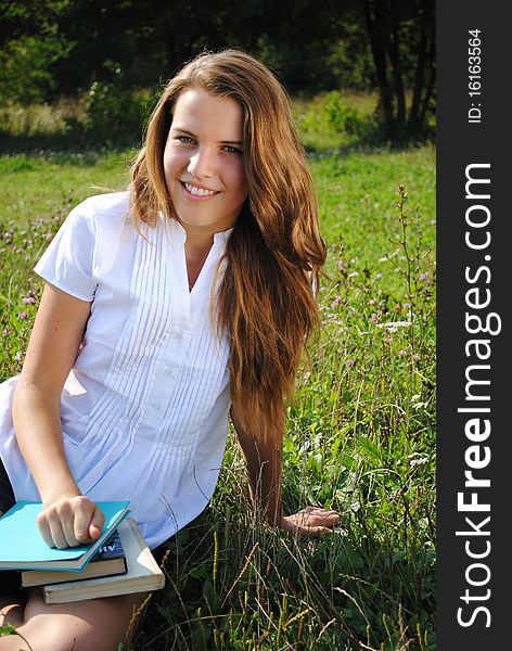 Beautiful student girl is seating on the grass with books and smiling. Beautiful student girl is seating on the grass with books and smiling