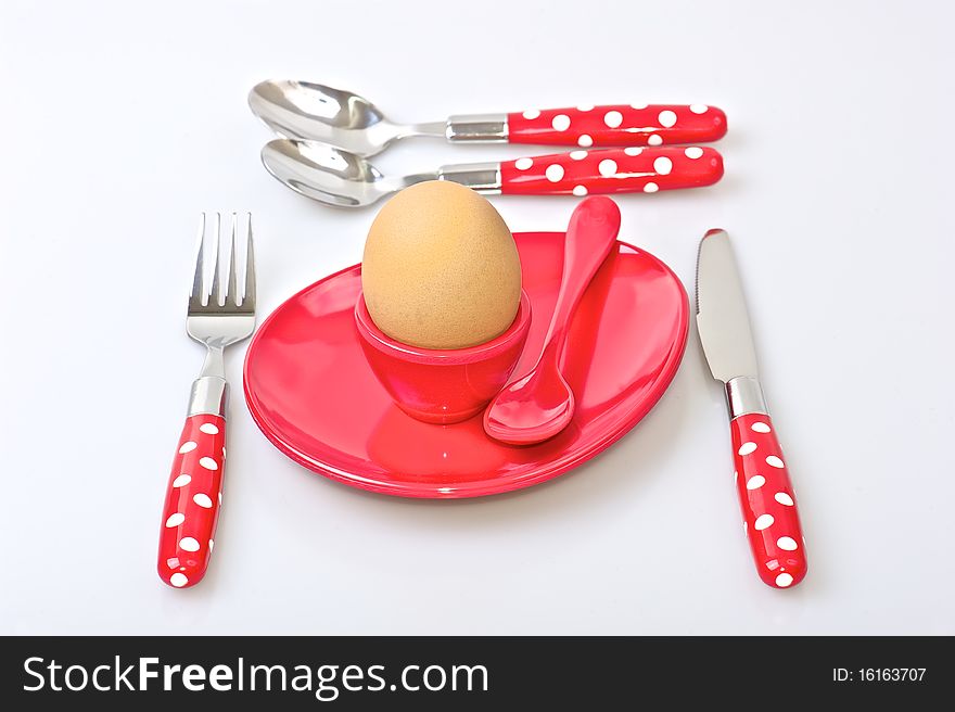 Table set for breakfast with red and white polka dot cutlery, brown egg and red egg cup and  saucer