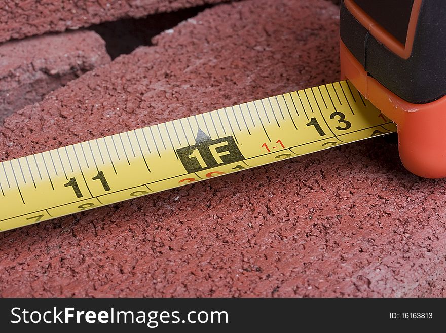 Orange tape measure on a red brick.