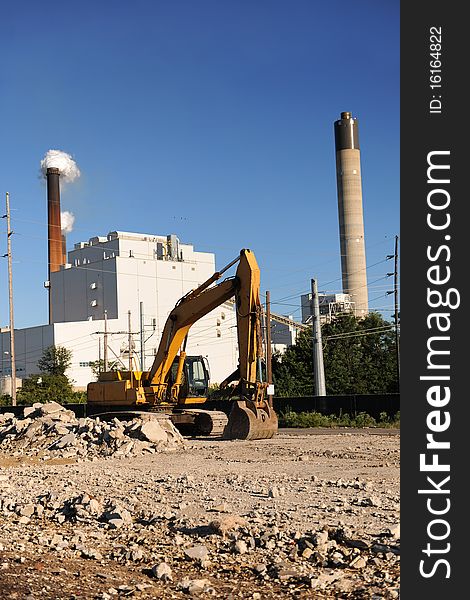 Industrial site with bulldozer in foreground and factory with smokestacks in background