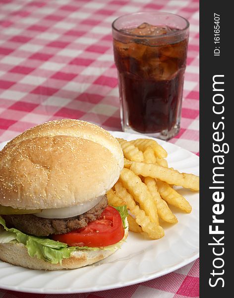 A freshly cooked hamburger and fries meal on a checkered tablecloth. A freshly cooked hamburger and fries meal on a checkered tablecloth.