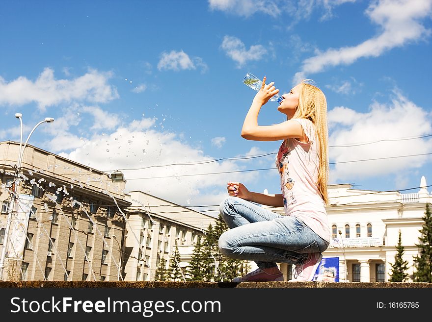 Young attractive girl drinking water, against blue sky