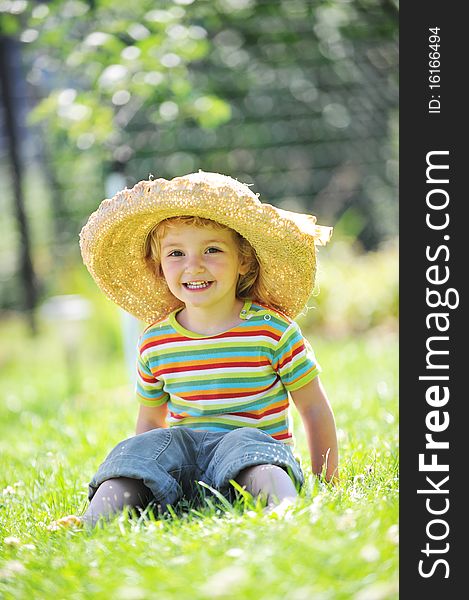 Little girl in straw hat sitting on green grass
