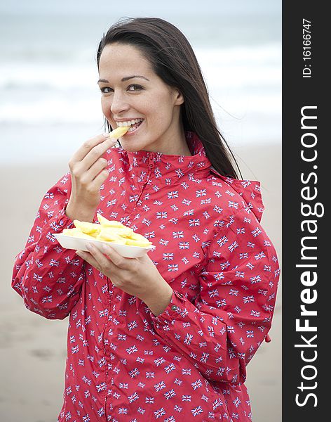 Woman wearing Union Jack raincoat eating chips at the beach. Woman wearing Union Jack raincoat eating chips at the beach