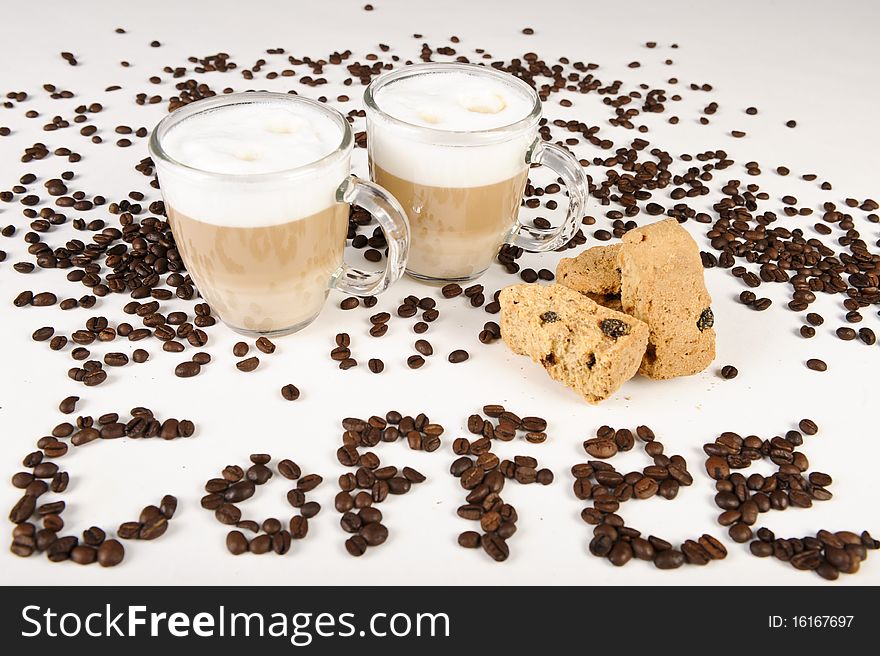 Two cups of freshly brewed latte macchiato standing between some coffee beans, and with a couple of rusks.