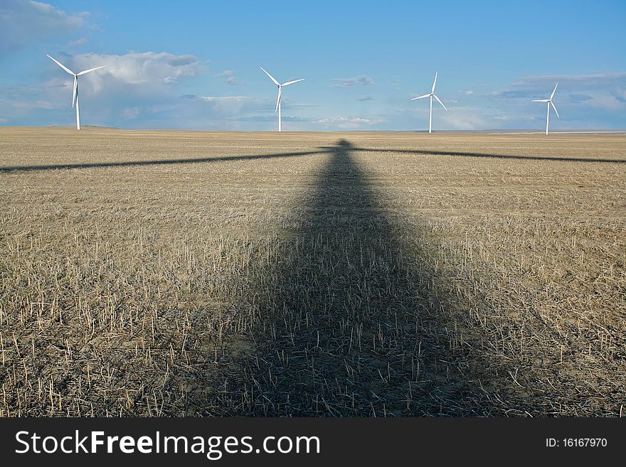 Shadow of wind turbine on stubble field with row of turbines in the background. Shadow of wind turbine on stubble field with row of turbines in the background