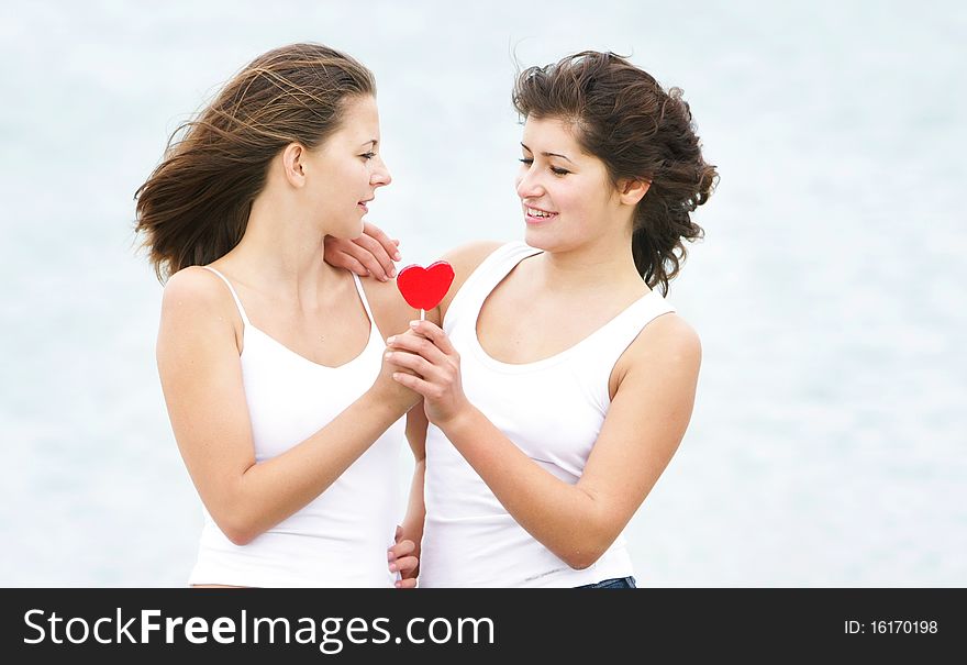 Two girls with heart-shaped candy on natural background. Two girls with heart-shaped candy on natural background