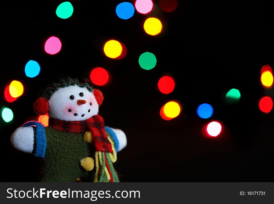 An old fashioned, hand made, snowman ornament in front of holiday lights