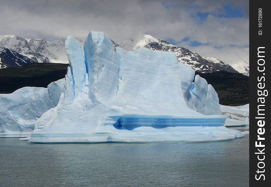 Iceberg floating in the water with mountain backdrop