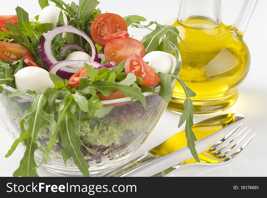 Fresh green vegetable salad with mozzarella in a transparent bowl over white background