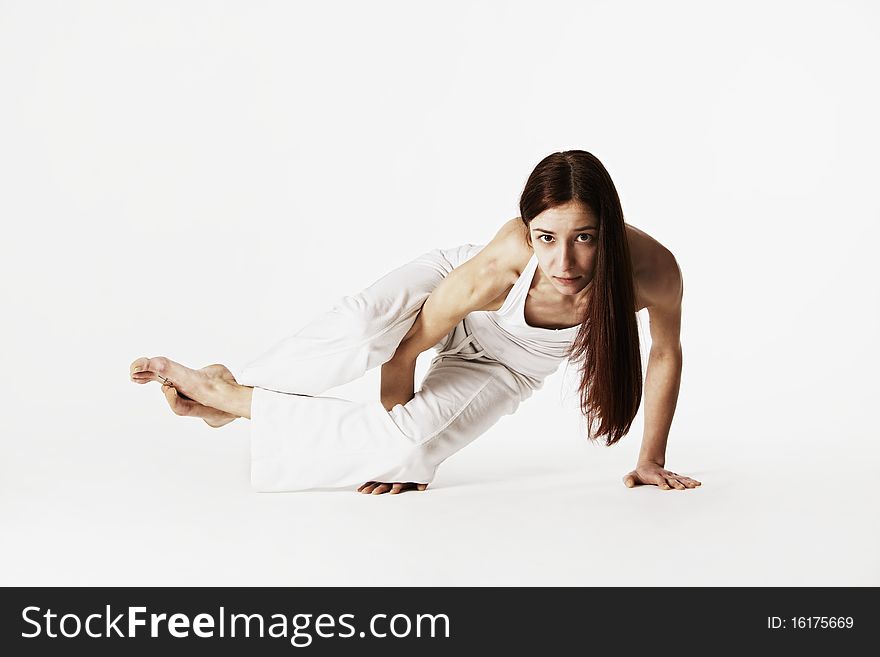 Young lady practicing sideways crow yoga posture (Ashtavakrasana) in white clothes on white background, high-key image. Young lady practicing sideways crow yoga posture (Ashtavakrasana) in white clothes on white background, high-key image.