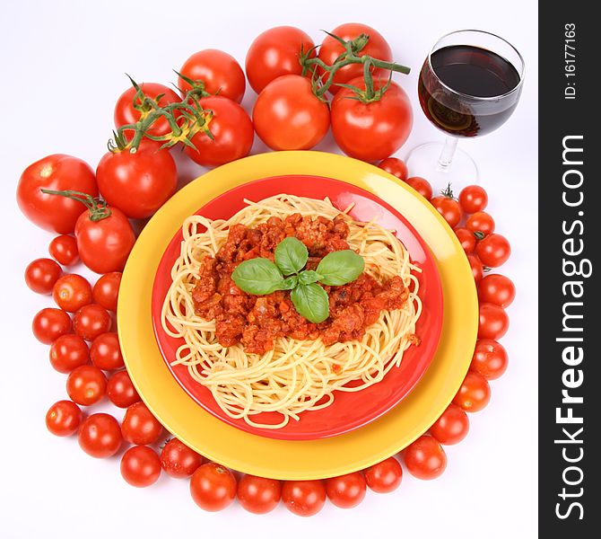 Spaghetti Bolognese on a plate decorated with fresh basil, some tomatoes and cherry tomatoes, and a glass of red wine