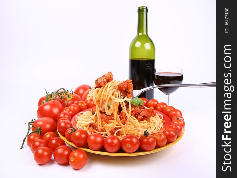 Spaghetti Bolognese being eaten with a fork from a plate, decorated with fresh basil, some regular tomatoes and cherry tomatoes, and some red wine