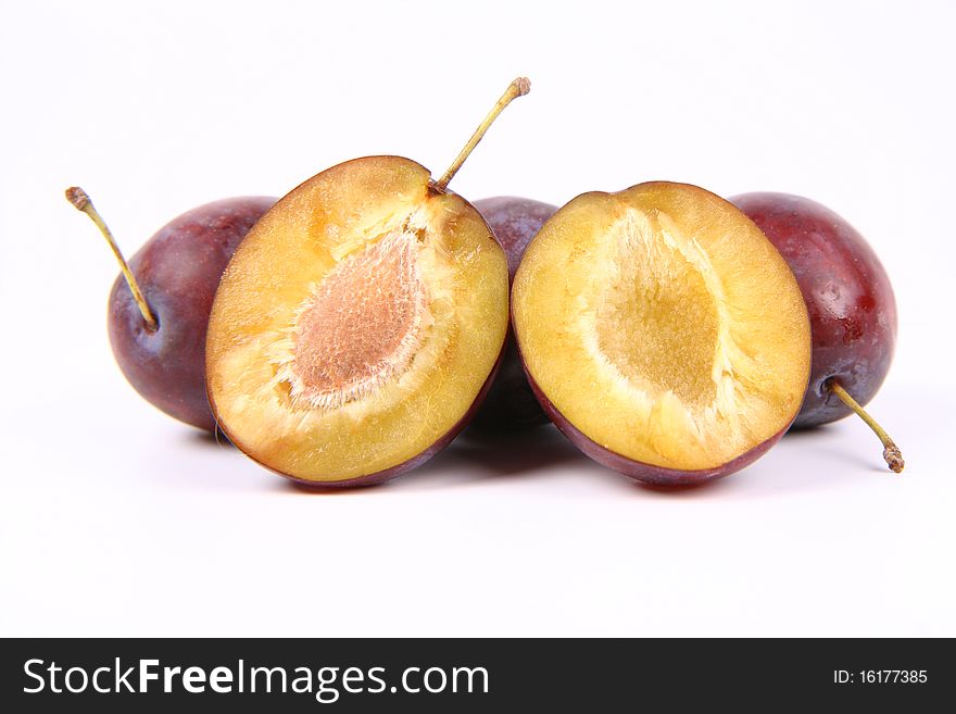 Plums on white background - one cut in half with a pit visible