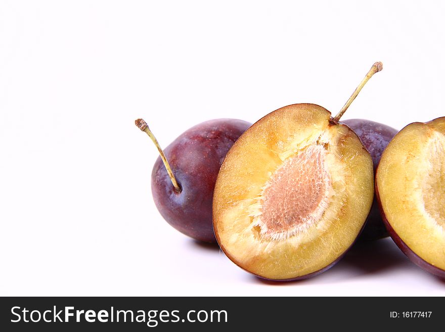 Plums on white background - one cut in half with a pit visible - with space for text. Plums on white background - one cut in half with a pit visible - with space for text