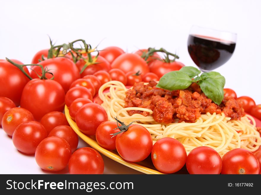 Spaghetti Bolognese on a plate decorated with fresh basil, some tomatoes and cherry tomatoes, and a glass of red wine
