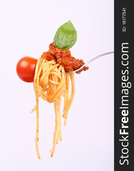 Spaghetti with sauce bolognese hanging on a fork with a cherry tomato, decorated with fresh basil. Spaghetti with sauce bolognese hanging on a fork with a cherry tomato, decorated with fresh basil