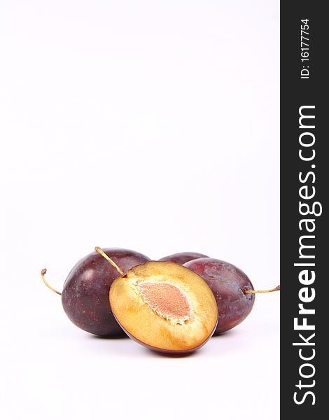 Plums on white background - one cut in half with a pit visible - with space for text. Plums on white background - one cut in half with a pit visible - with space for text