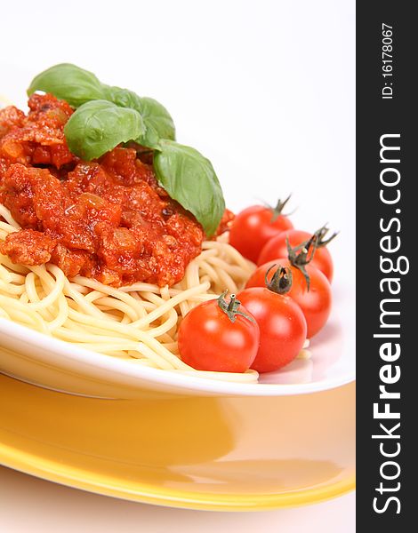 Spaghetti Bolognese on a plate decorated with fresh basil and cherry tomatoes in close up