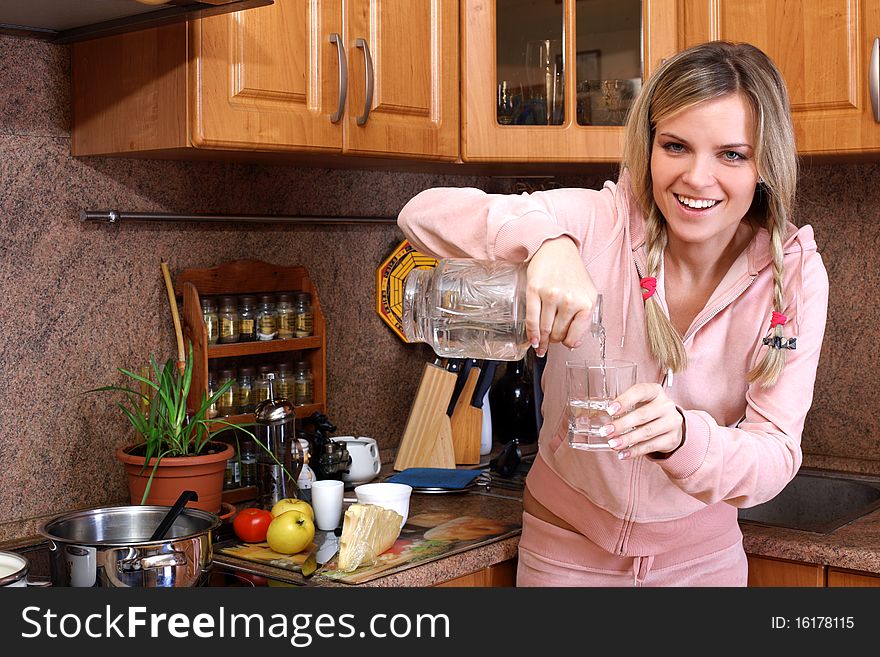Woman cooking dinner and holding glass with clear water in the kitchen
