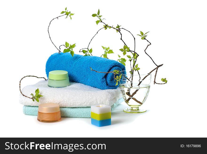 Stacked towels with cosmetic cream,burn candle and young green twigs on white. Stacked towels with cosmetic cream,burn candle and young green twigs on white