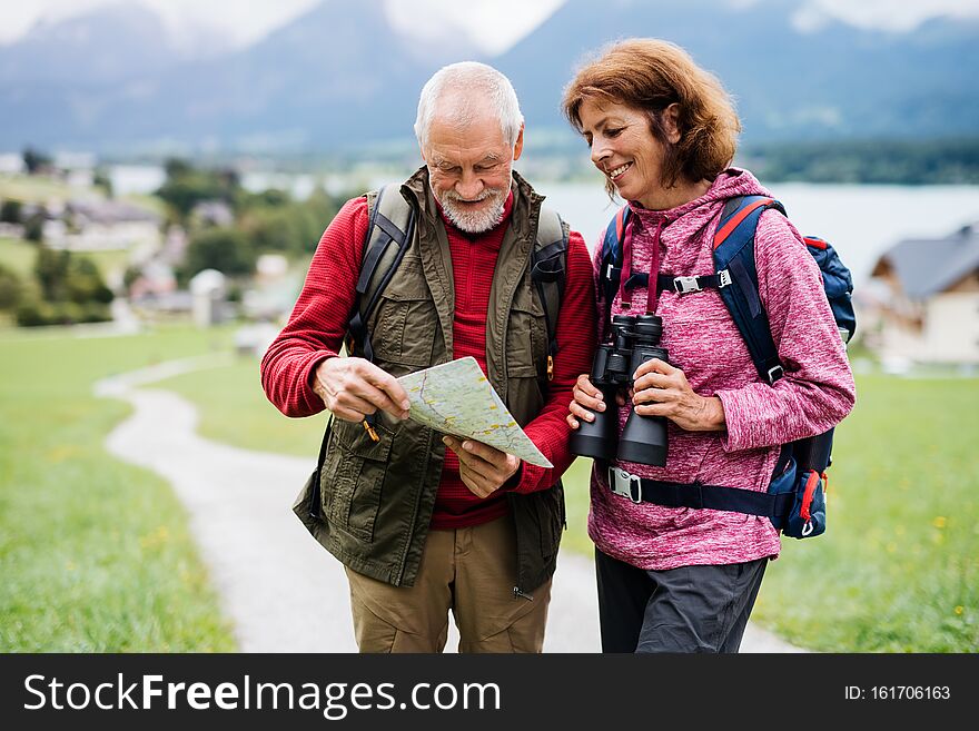 Senior pensioner couple with hiking in nature, using binoculars and map.