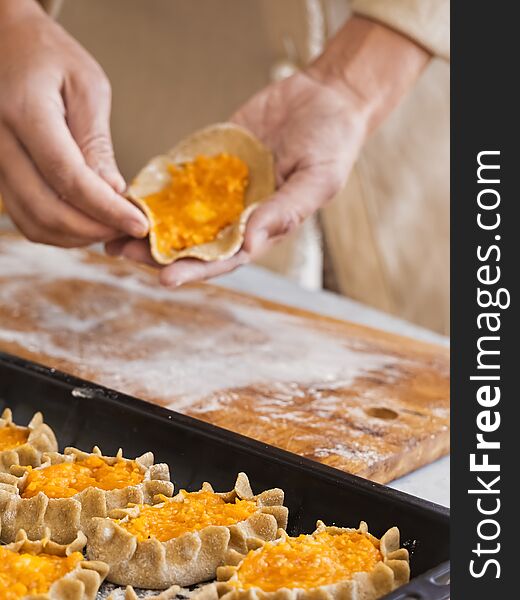 Stage of preparation of Karelian pies. Pies are located on a baking sheet, ready for baking. In the background, a woman is preparing pies. Dish of national cuisine - piirakka. Close-up