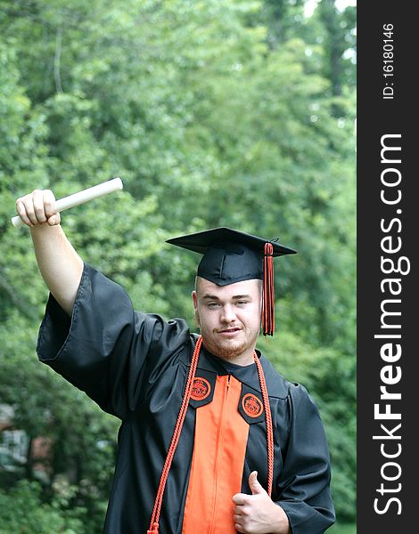 Young man in cap and gown holding diploma in air, graduating from college. Young man in cap and gown holding diploma in air, graduating from college