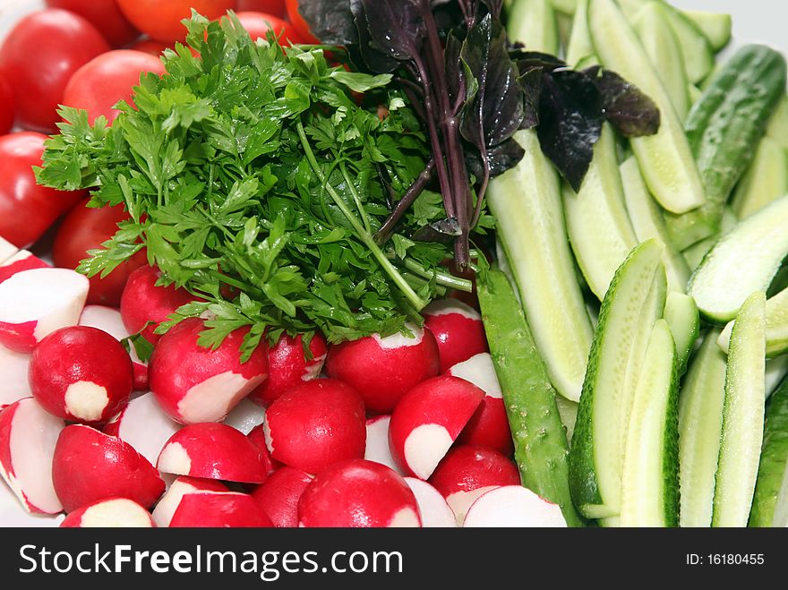 Fresh vegetables on a dish - a garden radish, tomatoes, cucumbers and greens