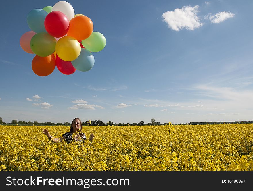 Girl with colorful balloons in canola field