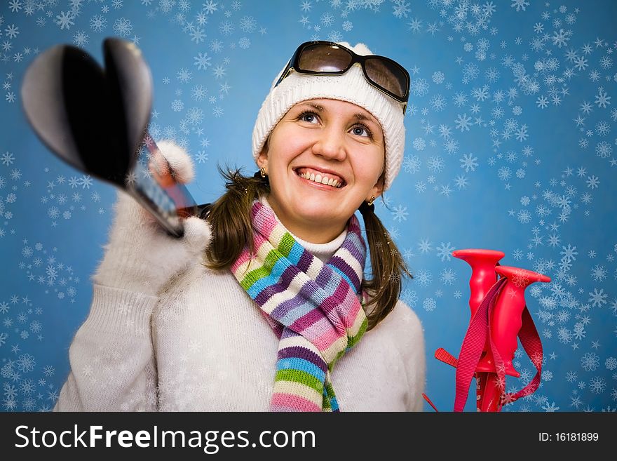 Portrait the beautiful woman in a cap with ski sticks in hands on a blue background. Portrait the beautiful woman in a cap with ski sticks in hands on a blue background