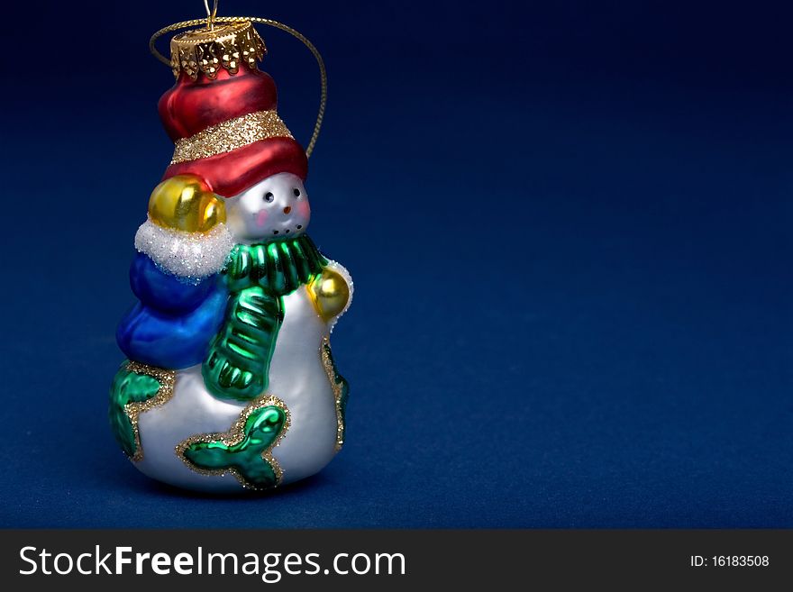 Closeup of a glass snowman ornament on blue background.