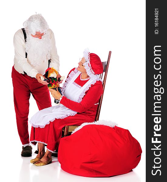 Mr. and Mrs. Santa Clause admiring a doll before putting it into Santa's sack. Isolated on white. Mr. and Mrs. Santa Clause admiring a doll before putting it into Santa's sack. Isolated on white.