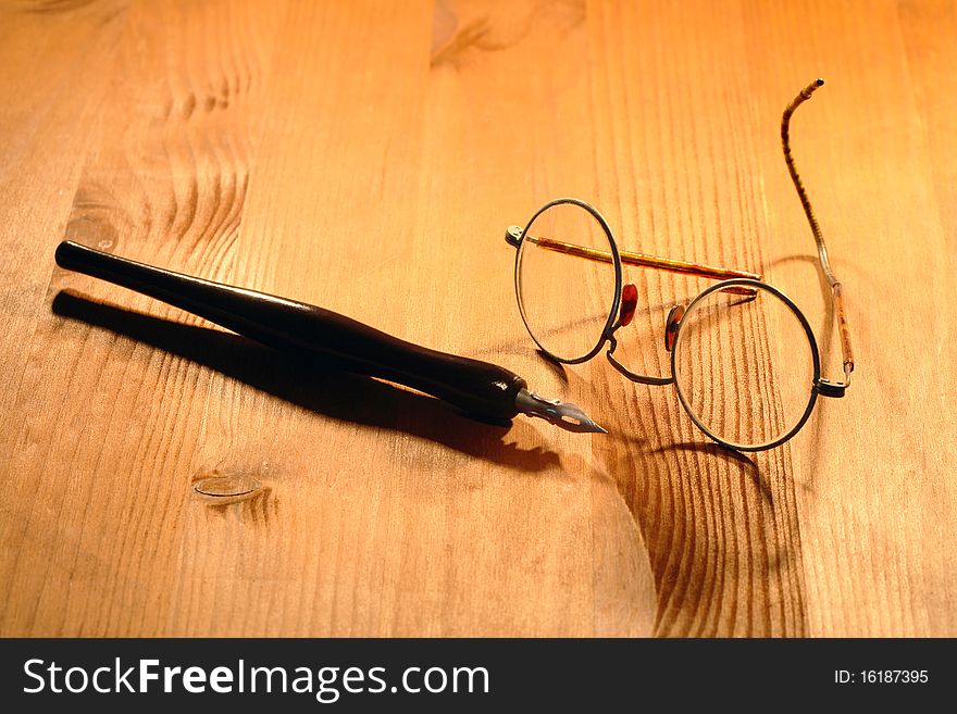 Old spectacles and ink pen lying on nice wooden background. Old spectacles and ink pen lying on nice wooden background