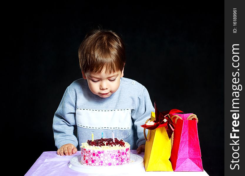 Cute three year old baby celebrating his birthday and blowing off the candles on the cake. Cute three year old baby celebrating his birthday and blowing off the candles on the cake