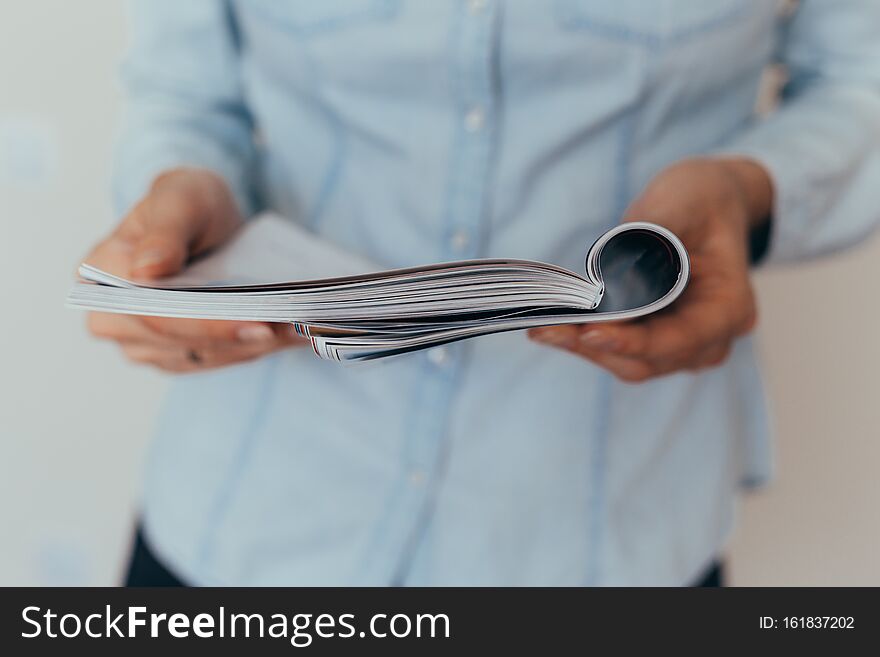 Beautiful female hands are holding an open book or magazine in a room on against a light wall. Beautiful female hands are holding an open book or magazine in a room on against a light wall