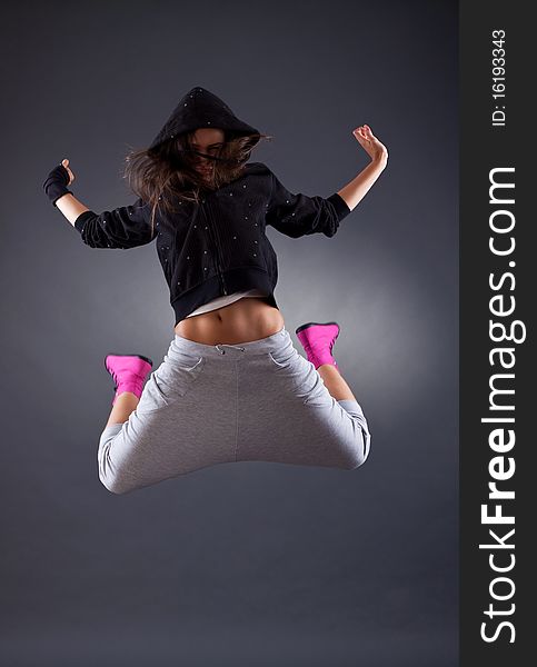 Young female dancer jumping on the grey background