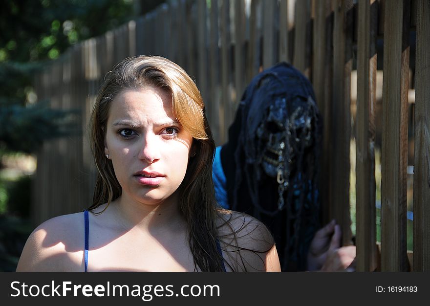 A girl stands with scared look while a man stands behind her with a scary mask. A girl stands with scared look while a man stands behind her with a scary mask.