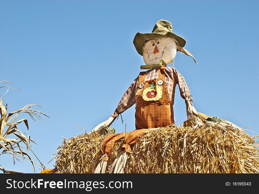 A fall scarecrow sitting on a bail of hay with blue sky background, copy space. A fall scarecrow sitting on a bail of hay with blue sky background, copy space