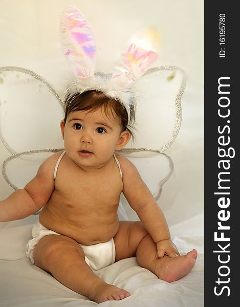 Cute baby sitting and smiling with angel wings and colorful bunny ears