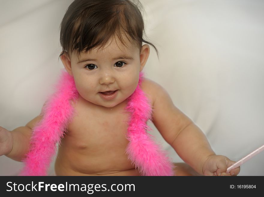 Naked baby girl sitting and smiling with pink feather neck wear