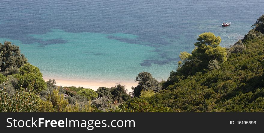 A beautiful panoramic view of the sea on the beautiful island of Skiathos, Greece. The water near the bay is a turquoise blue and there is a small fishing boat on the right. A beautiful panoramic view of the sea on the beautiful island of Skiathos, Greece. The water near the bay is a turquoise blue and there is a small fishing boat on the right.