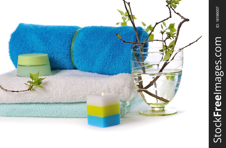 Stacked towels with cosmetic cream,burn candle and young green twigs on white. Stacked towels with cosmetic cream,burn candle and young green twigs on white