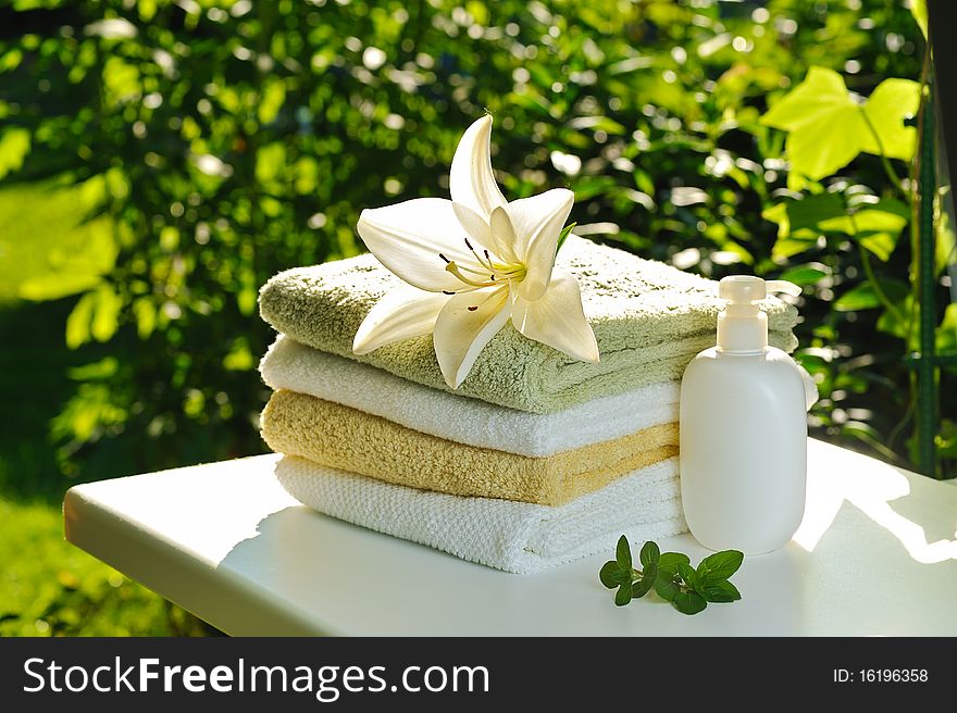 Backloghting with sun white lily on stack of towels against green summer background. Backloghting with sun white lily on stack of towels against green summer background