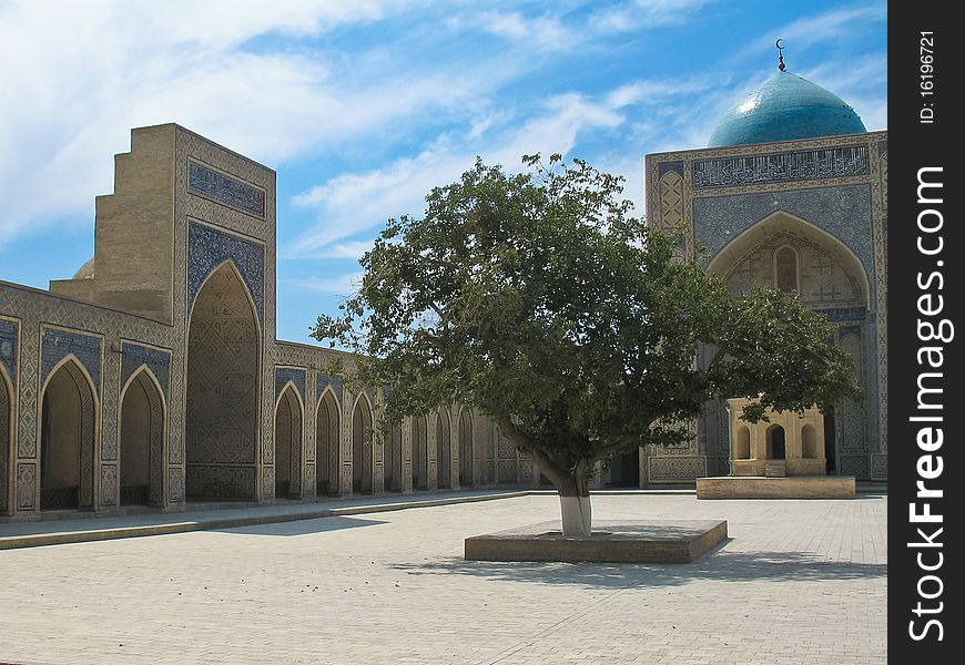 The area inside the madrasa. Arches, tree and blue dome against the blue sky. The area inside the madrasa. Arches, tree and blue dome against the blue sky.