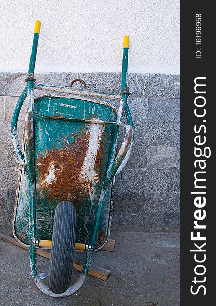 An old wheelbarrow leaning against a wall of a house under construction during a break