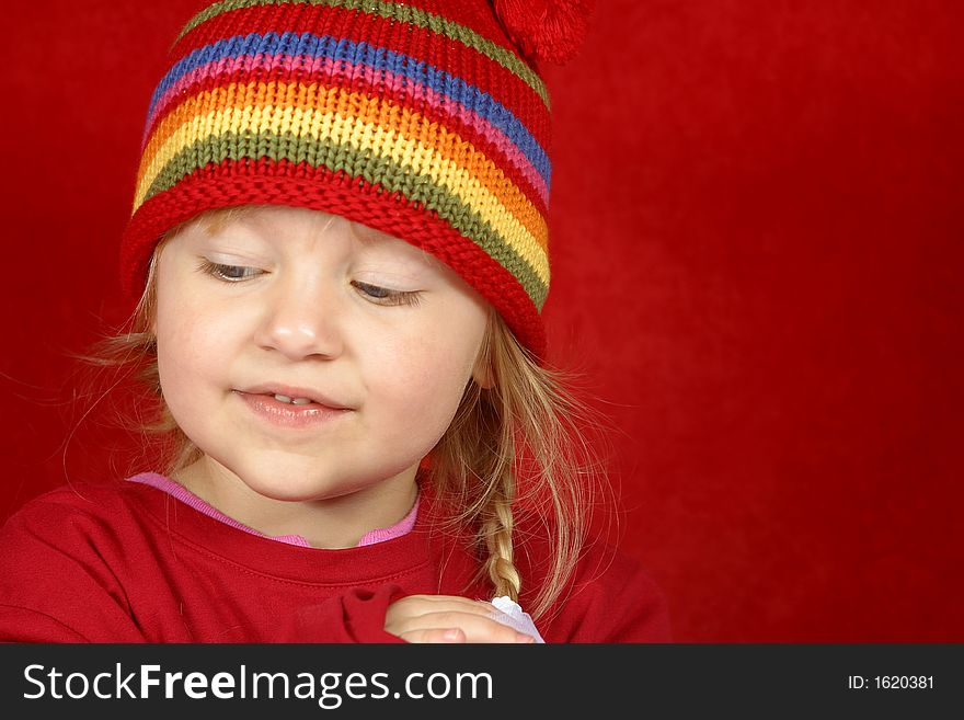 A cute little girl with a red and multi color-striped hat on a red background