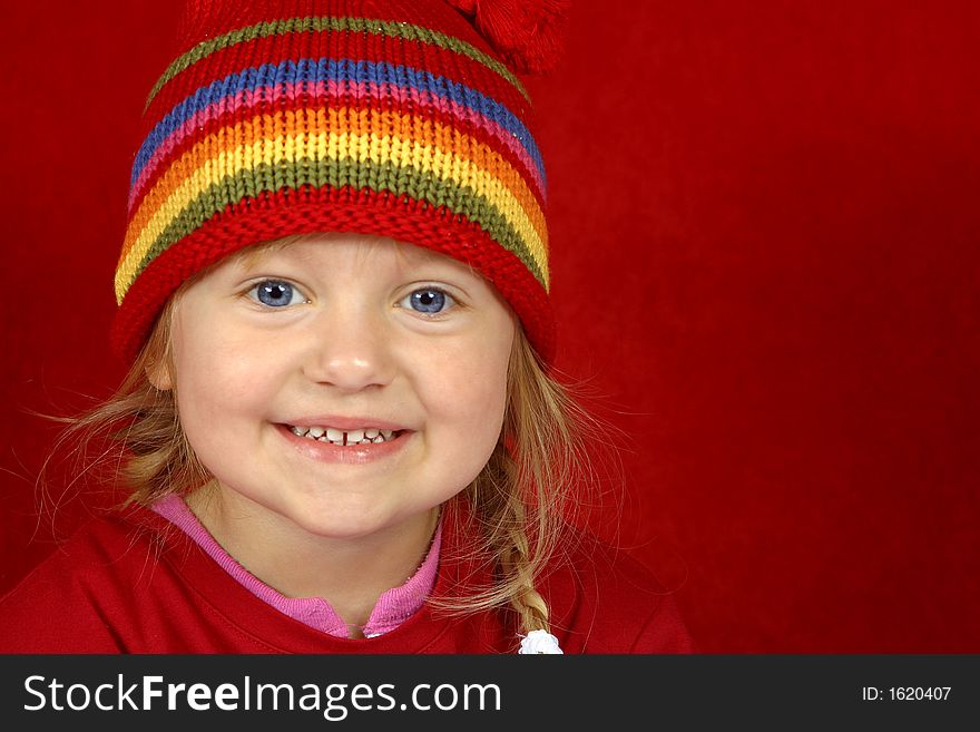 A cute little girl with a red and multi color-striped hat on a red background