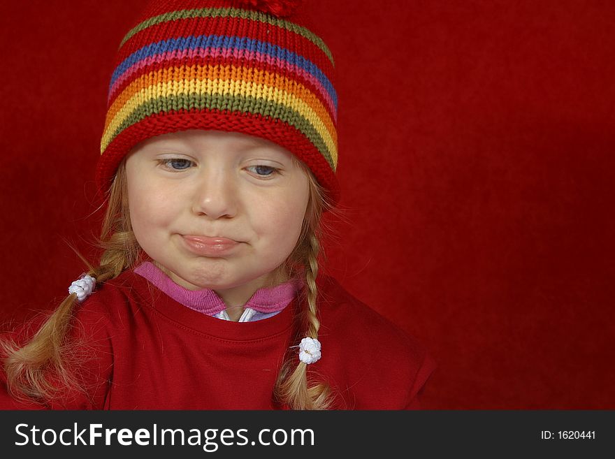 A cute little girl with a red and multi color-striped hat making silly faces