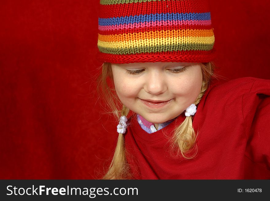 A cute little girl with a red and multi color-striped hat on a red background